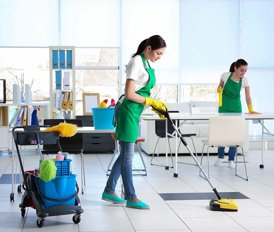 Two cleaners in green aprons cleaning an office